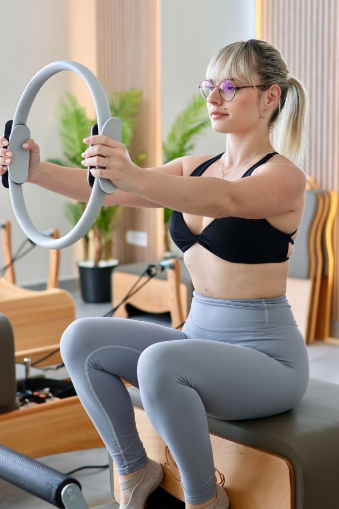 Vežbačica sedi uspravno i radi vežbu sa pilates krugom